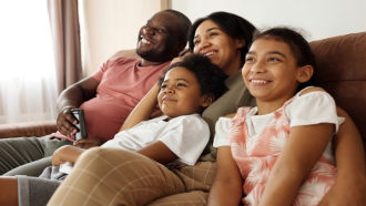 smiling family watches tv together on a couch