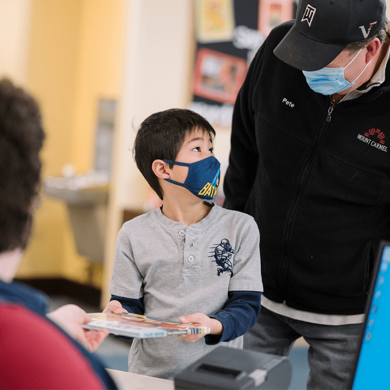boy looks at father while checking out a book at service desk