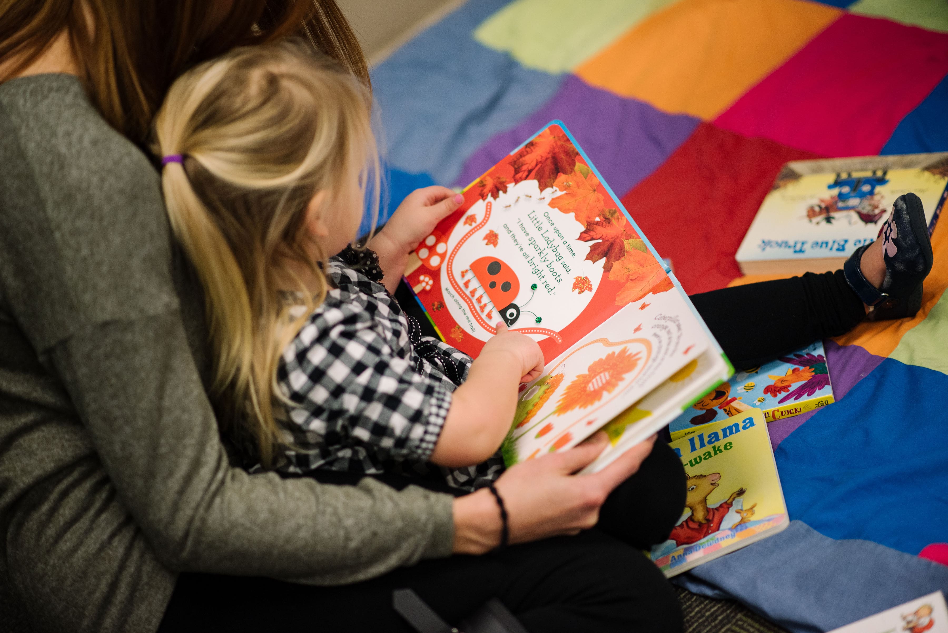 A child reads a book on the floor with her mother 