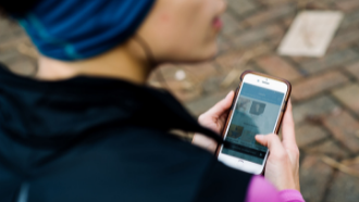 photo of the back of a  woman's head listening to headbuds looking at mobile phone