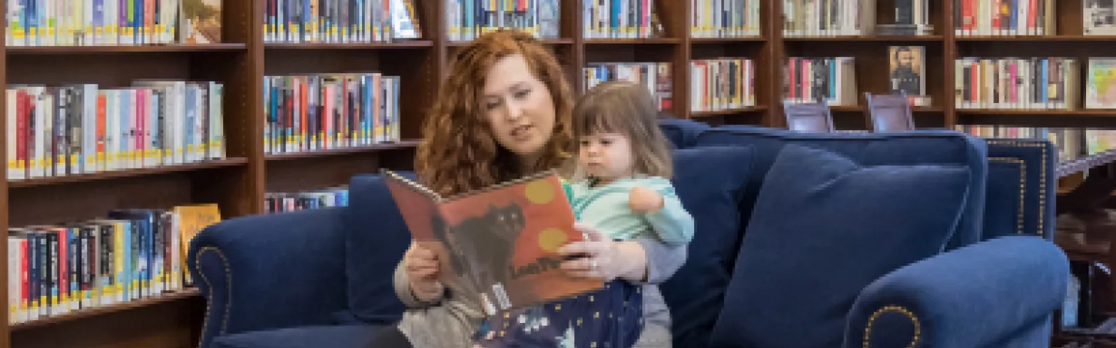 Woman reads to young child inside the library.